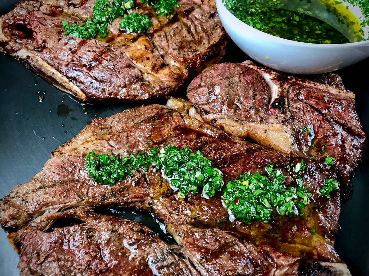 Closeup of grilled chuck steaks with chimichurri sauce on top.