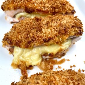 Baked chicken cordon bleu on a platter with cheese oozing out.
