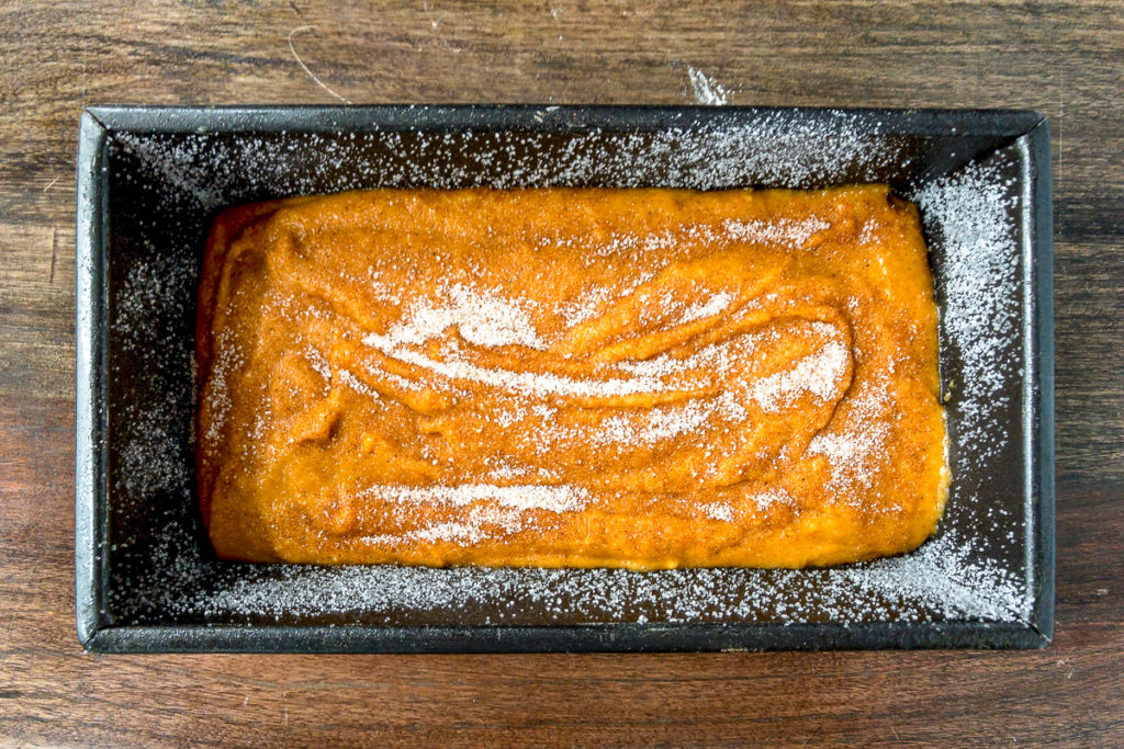 Pumpkin bread batter in a loaf pan topped with sugar.