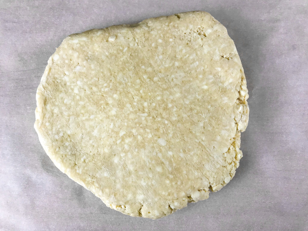 A disc of pie crust on parchment paper.