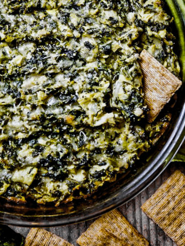 Cheesy spinach artichoke dip surrounded by crackers.