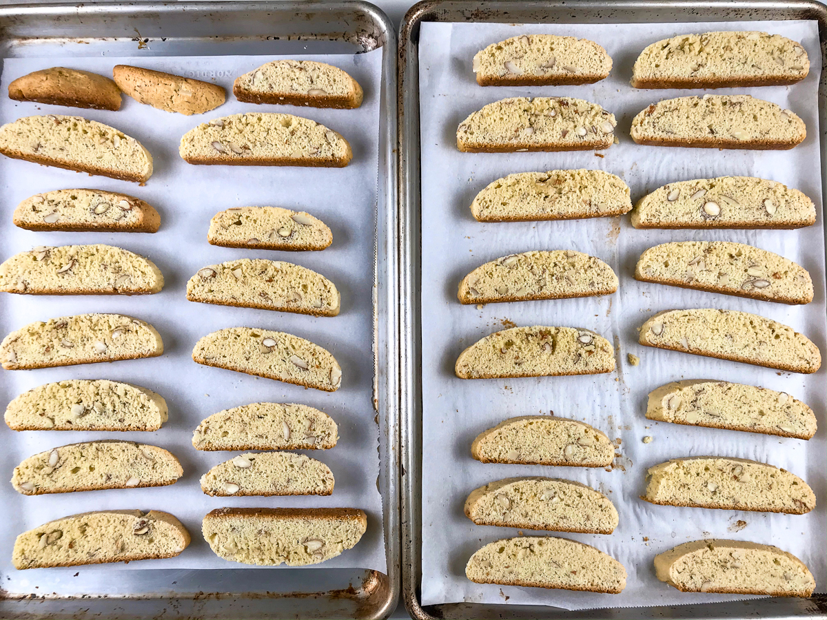 Sliced almond biscotti on two baking sheets.