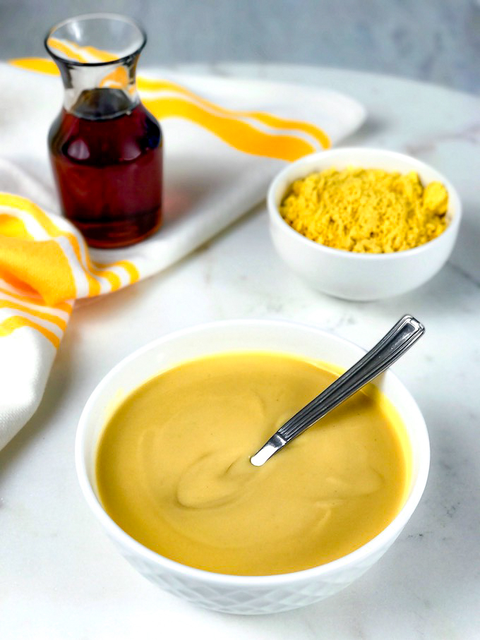 A bowl of mustard sauce with dry mustard and maple syrup in. the background.