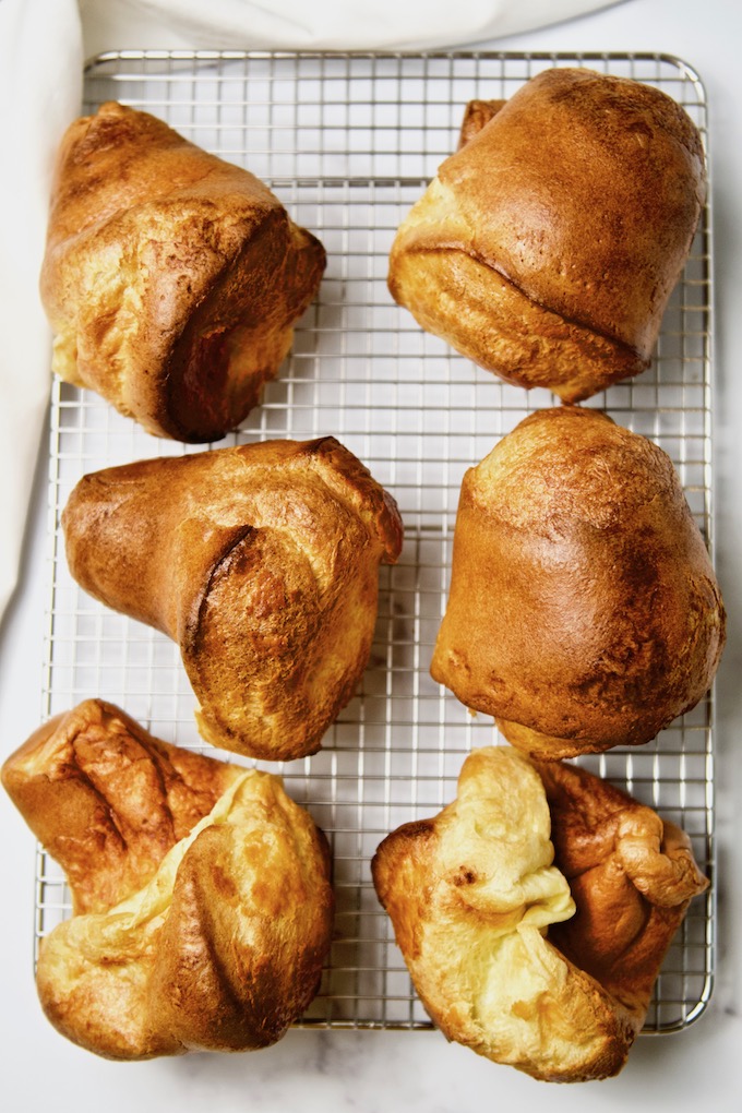 Six big golden popovers on a rack.