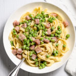 A bowl of fettuccine with peas and ham.