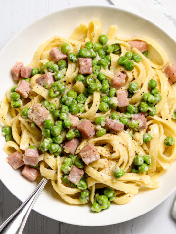 A bowl of fettuccine with peas and ham.