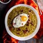 A bowl of split pea soup with bacon and a fried egg on top.
