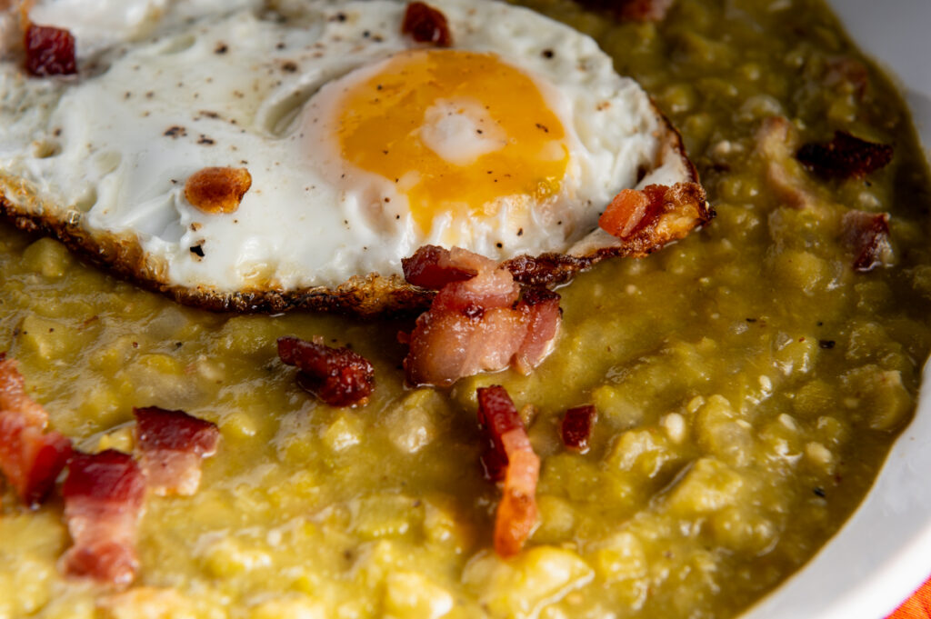 A fried egg on top of split pea soup with bacon bits.