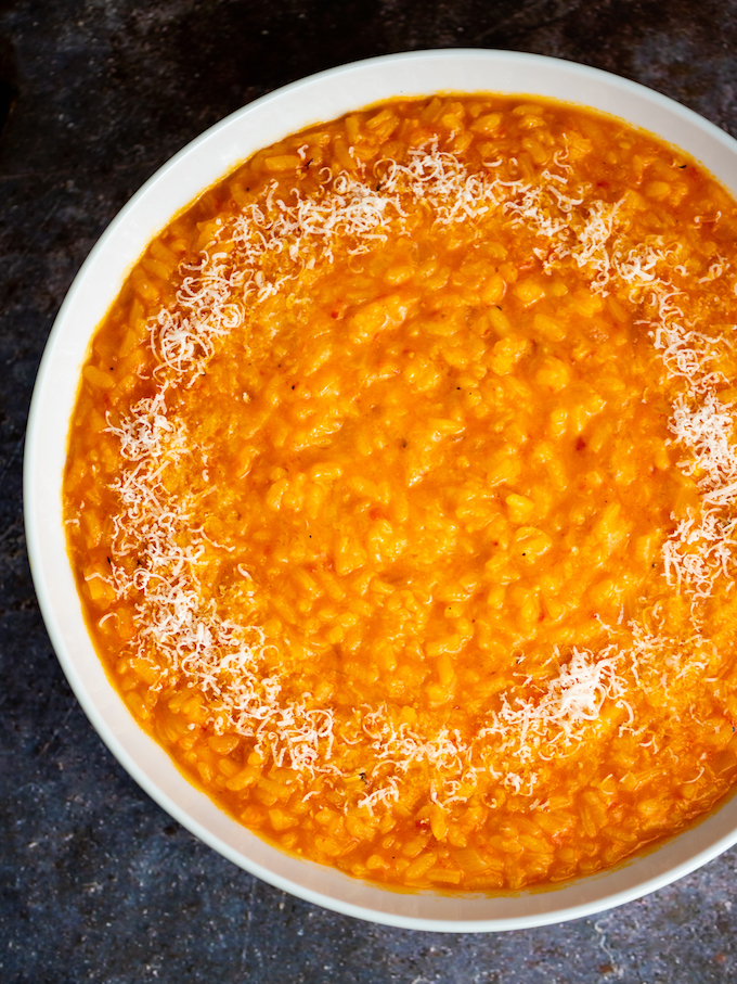 A bowl of red pepper risotto with some grated Parmesan.