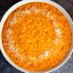 A bowl of red pepper risotto with some grated Parmesan.
