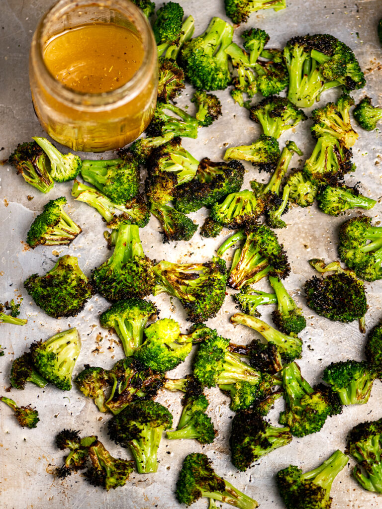 Charred broccoli tossed with Italian dressing on a baking sheet.
