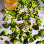 Charred broccoli tossed with Italian dressing on a baking sheet.