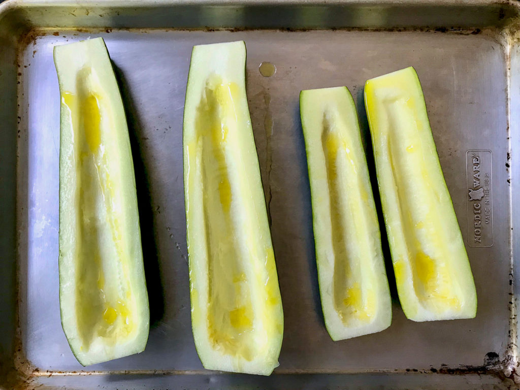 Four zucchini halves drizzled with olive oil on a baking sheet.