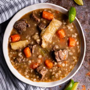 A bowl of beef barley soup with sliced limes.