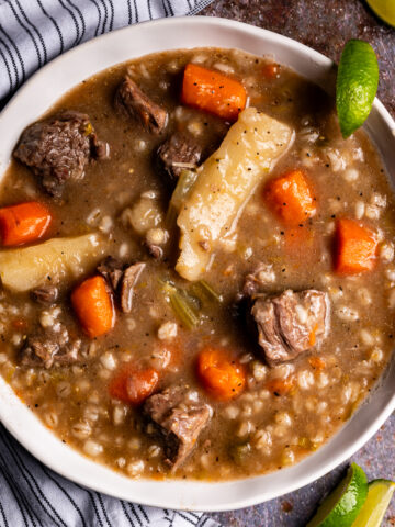 A bowl of beef barley soup with sliced limes.