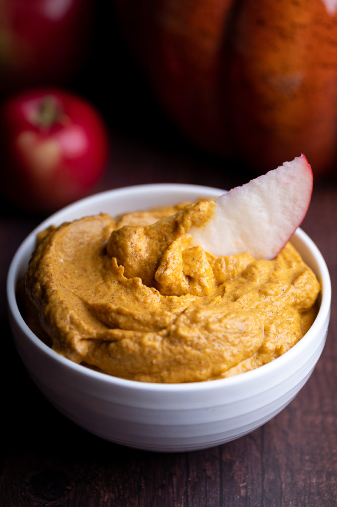 A white bowl with pumpkin dip with an apple slice in it.