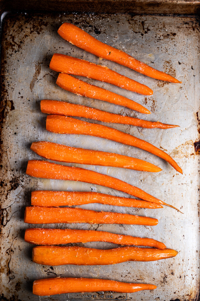 Carrots coated in butter on a baking sheet.