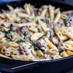 A cast iron skillet filled with creamy cheesy pasta with spinach and sausage.
