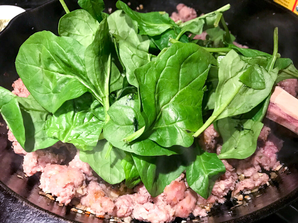 Adding spinach to sausage in a skillet.