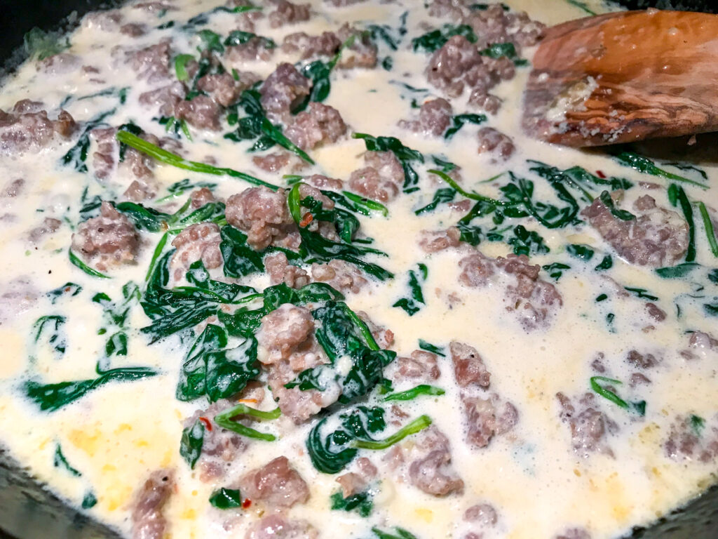 Mixing cream into the spinach and sausage in a skillet.