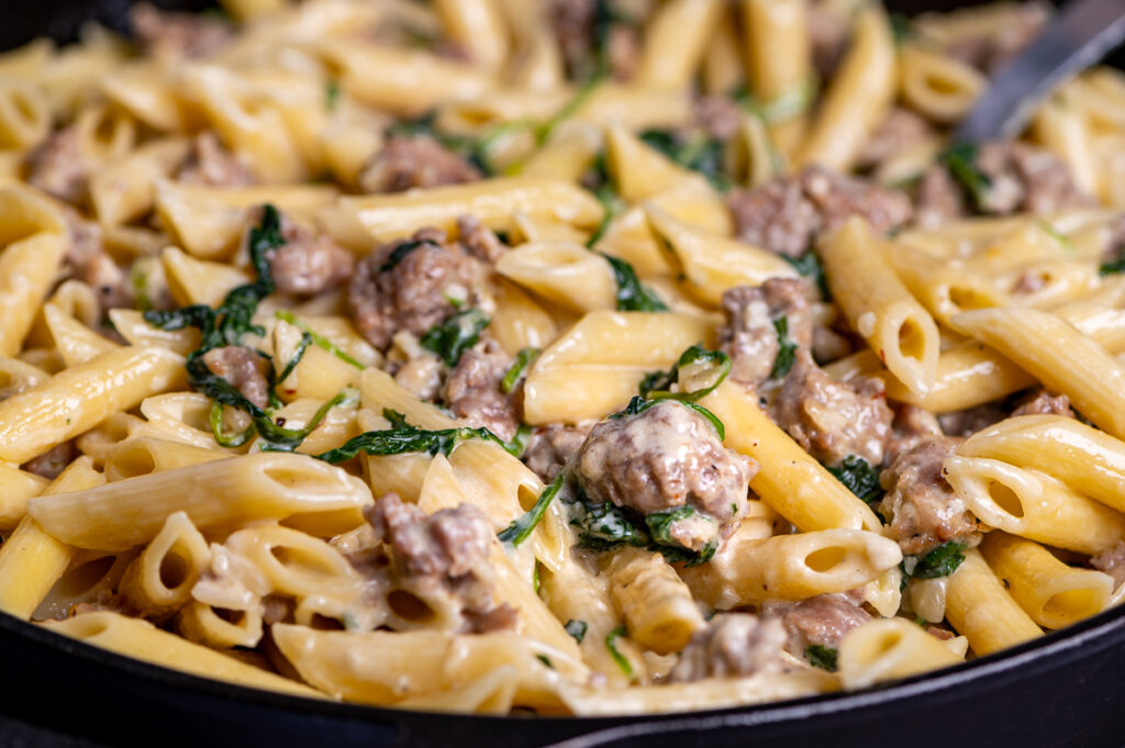 Closeup of pasta, sausage, and spinach tossed in a creamy sauce.