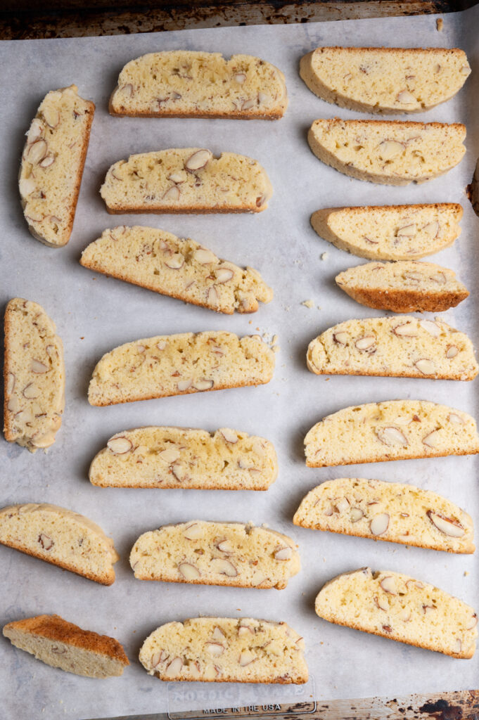 Sliced almond biscotti on two baking sheets.