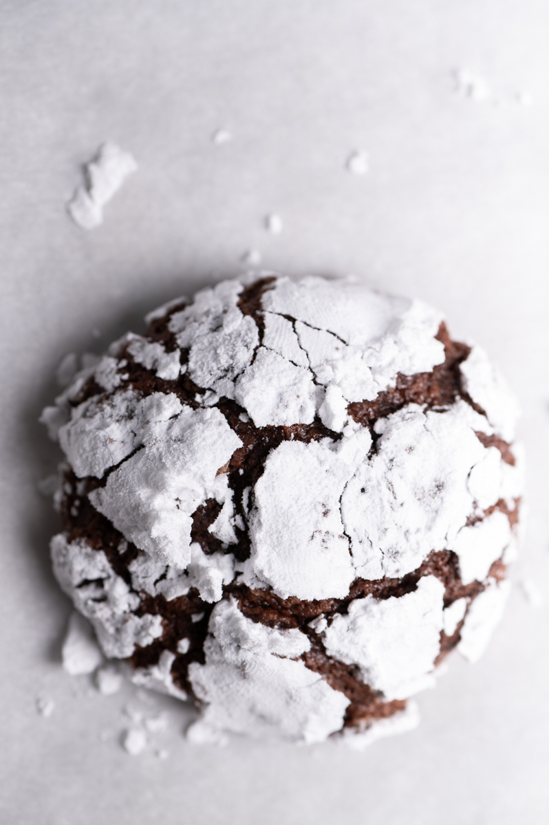 A single chocolate crinkle cookie on parchment paper.