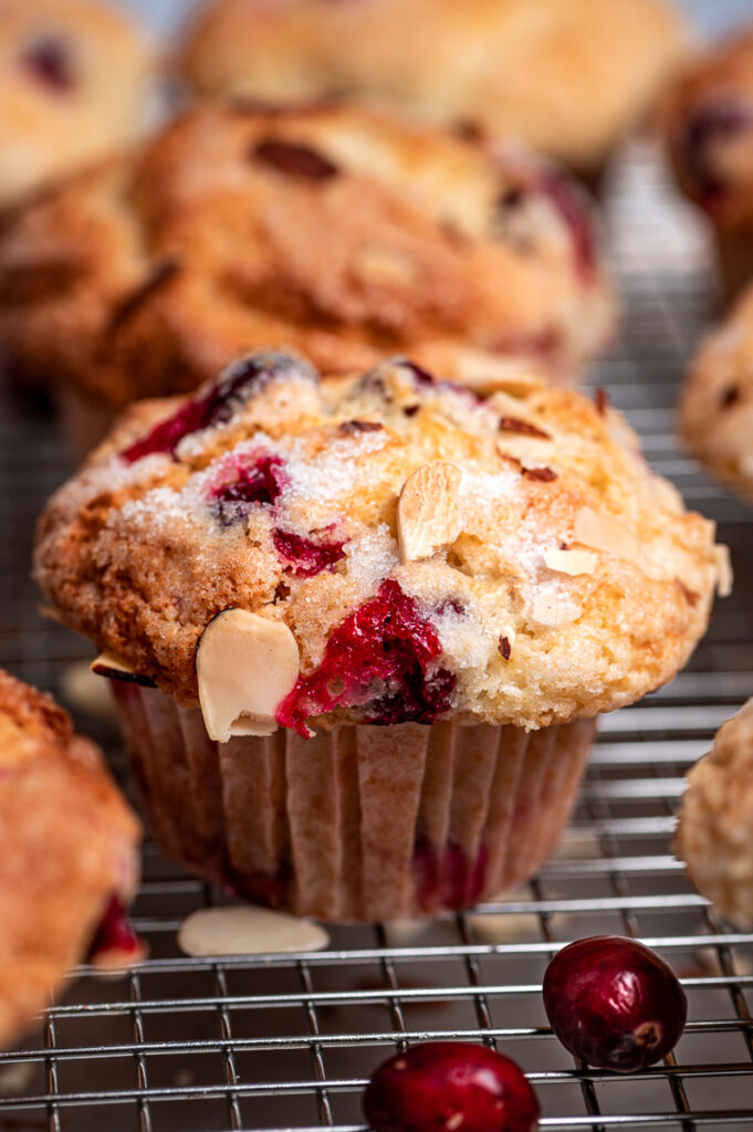 A cranberry muffin on a cooling rack with more in background.