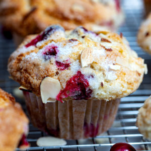 A cranberry muffin on a cooling rack with more in background.