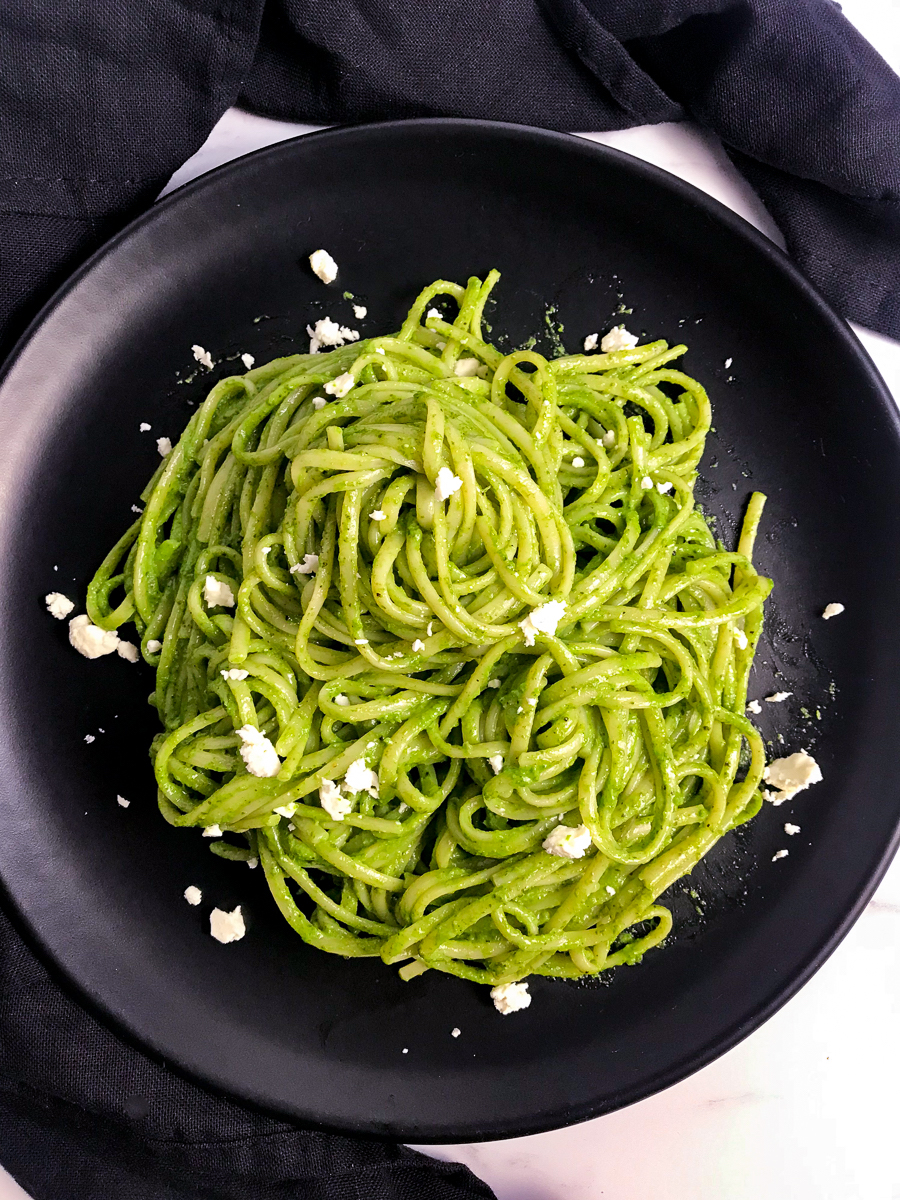 A black plate of pasta tossed with Peruvian pesto with bits of feta on top.
