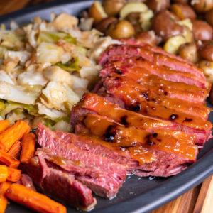 An angled view of a black tray with sliced corned beef, baby potatoes, sautéed cabbage, and roasted carrots.