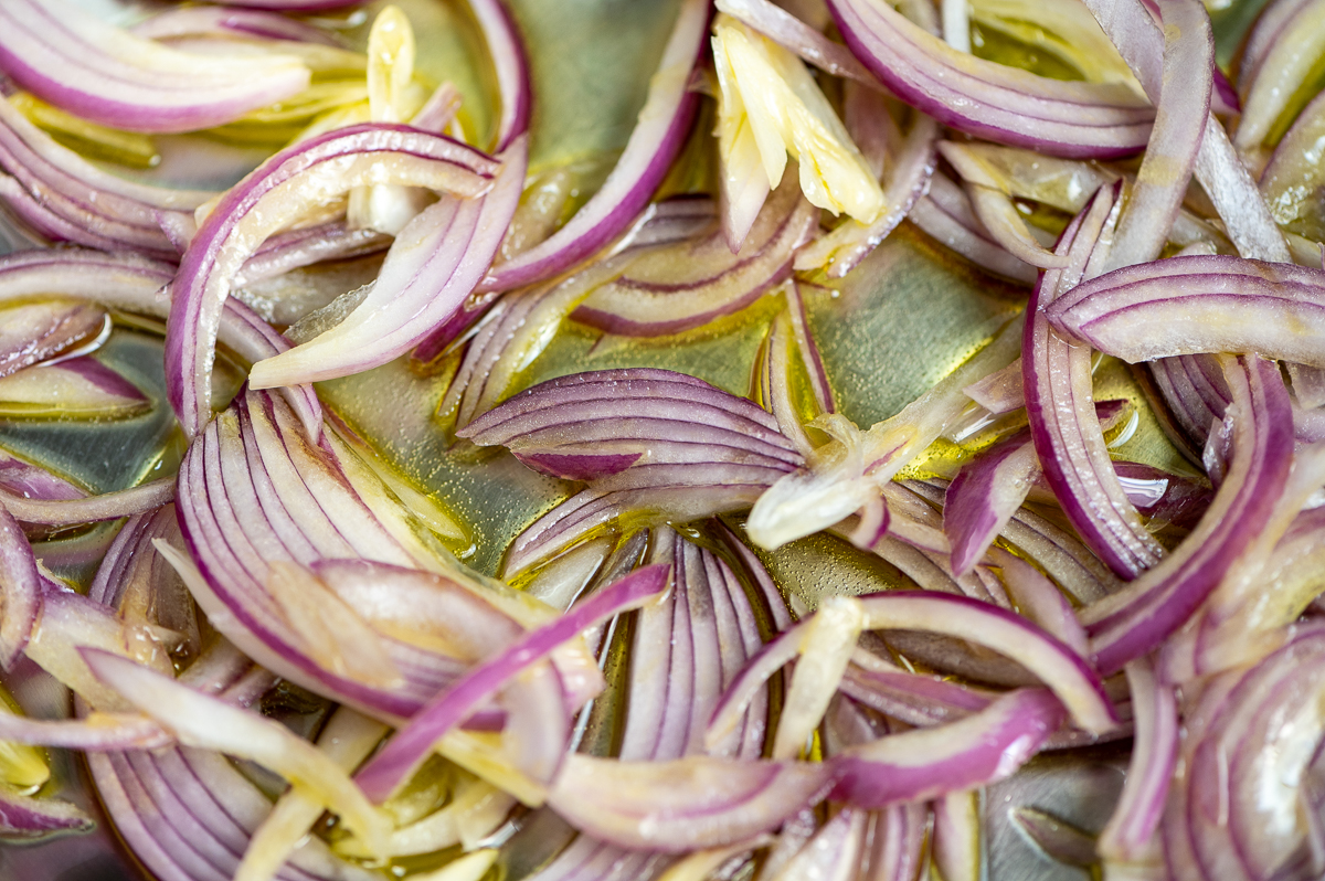 Red onions being sautéed in a pan.