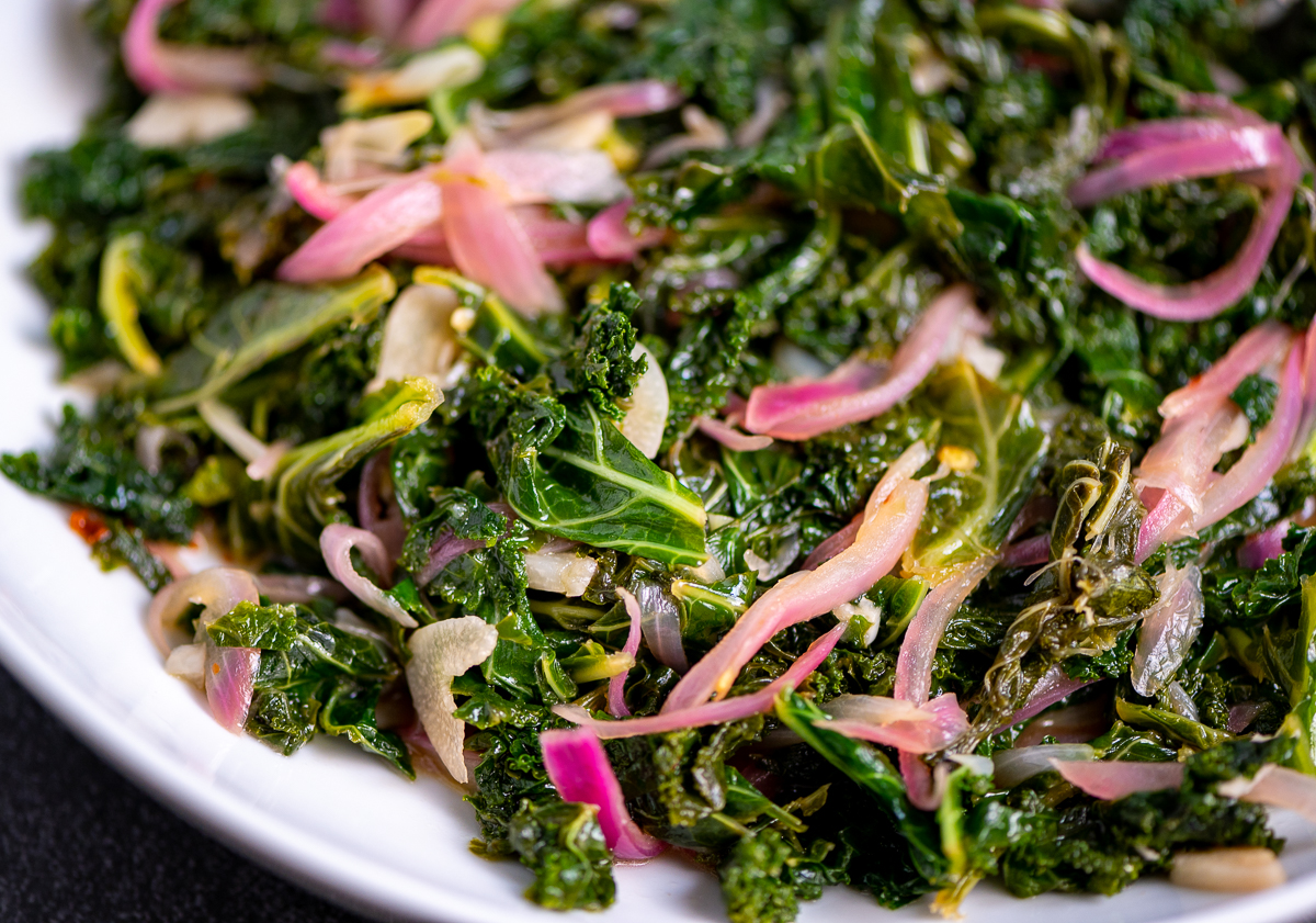 Sautéed kale with red onions in a white bowl.