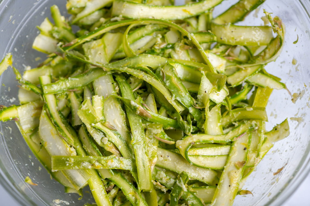 Asparagus strips in a bowl tossed with lemon dressing.