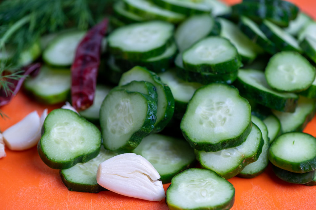 Sliced cucumbers with a few garlic cloves on a cutting board.