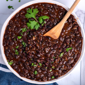 A white bowl of drunken black beans garnished with chopped cilantro.