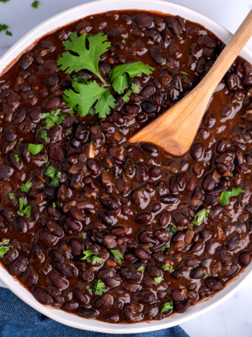 A white bowl of drunken black beans garnished with chopped cilantro.