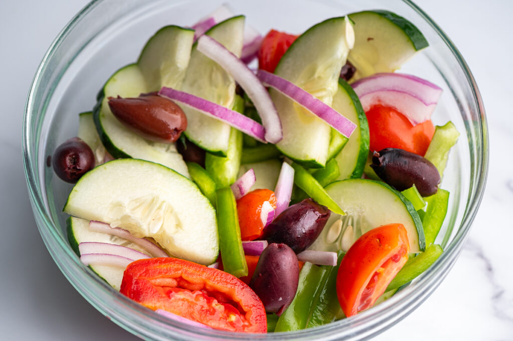 Tomatoes, cucumbers, olives, peppers and red onions in a bowl.