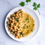 Chickpeas on one side of a white plate with a marinade on the other side.