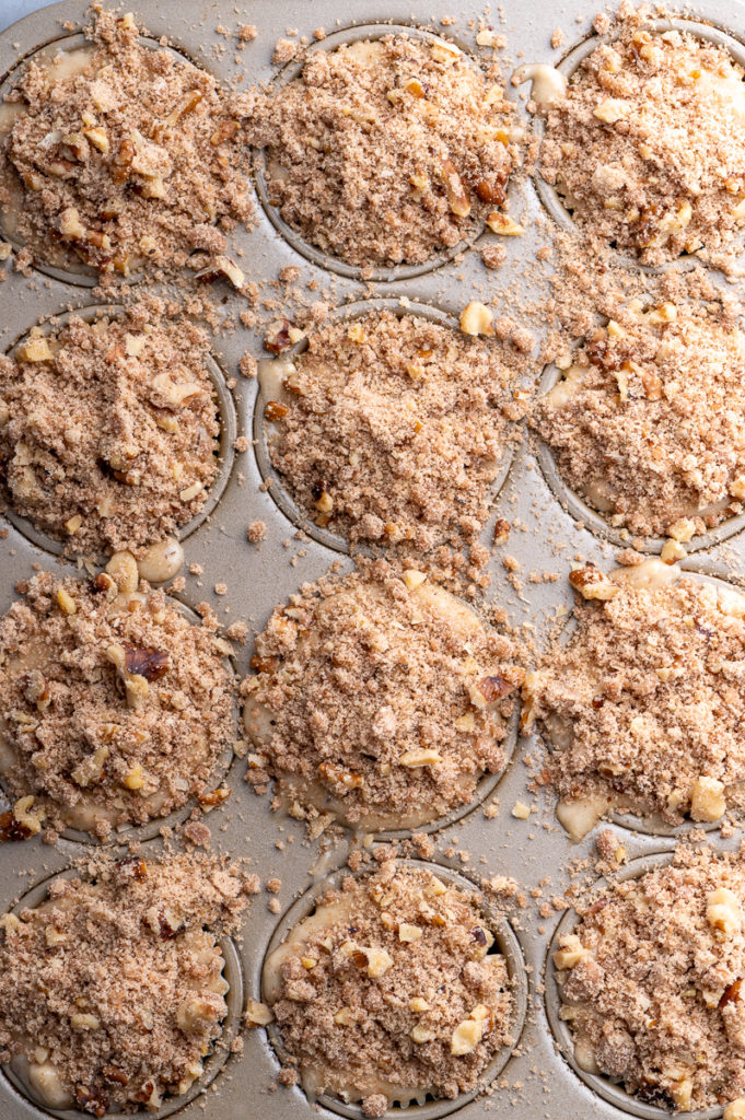 Twelve unbaked banana walnut streusel muffins in a muffin tin.