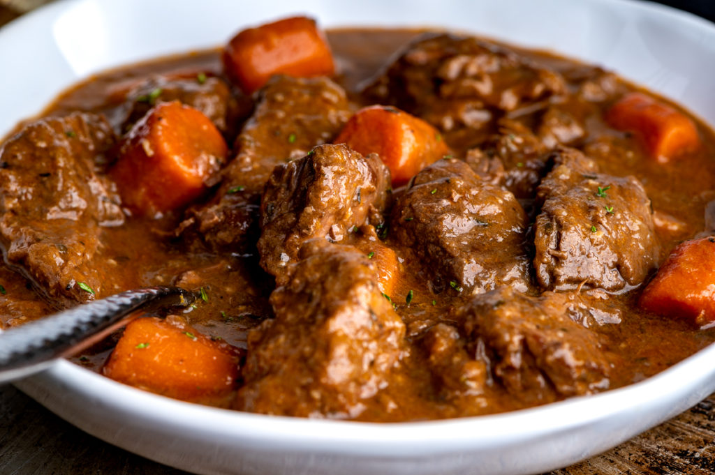 A white bowl with chunks of beef and carrots in gravy.