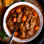 A white bowl of Guinness beef stew with crusty bread.