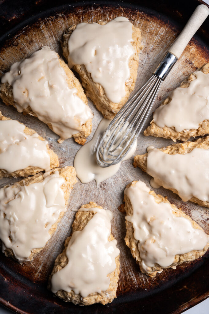 Eight iced maple scones in a circle with a whisk of icing.