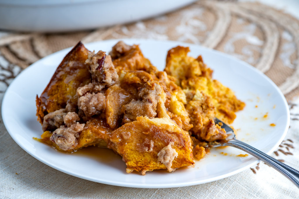 A serving of pumpkin French toast casserole on a white plate drizzled with maple butter.