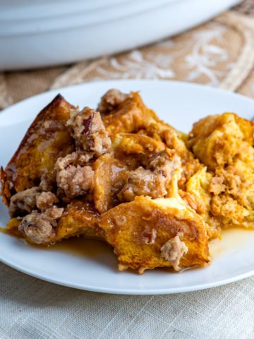 A serving of pumpkin French toast casserole on a white plate drizzled with maple butter.