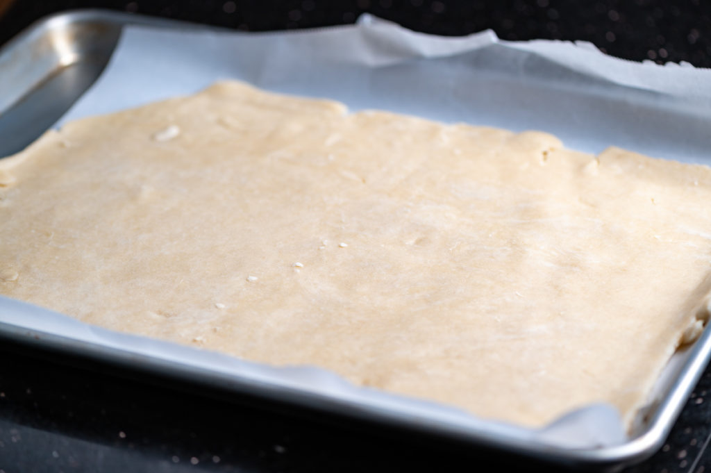 A pie crust shaped as a rectangle on a baking sheet.