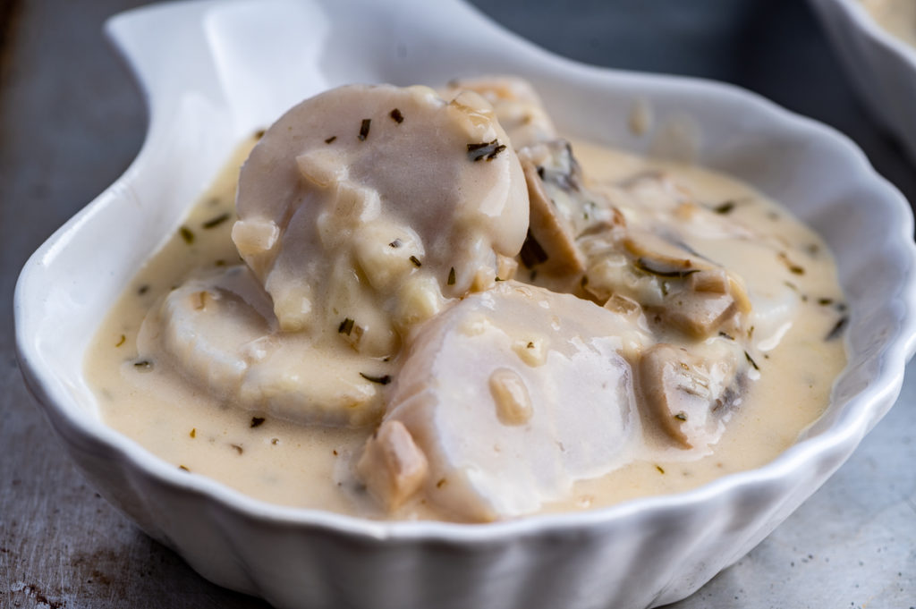 Scallops are coated in a creamy mushroom sauce in a white shell dish.