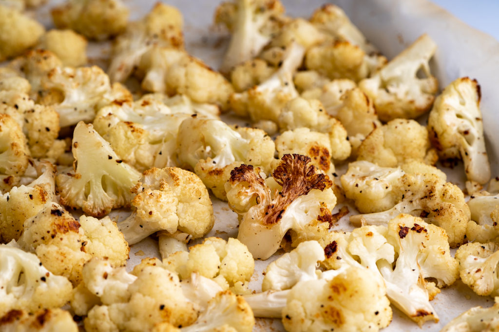 Roasted cauliflower scattered on a baking sheet.