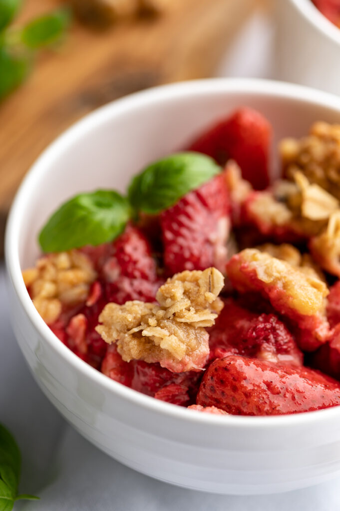 Strawberry crisp in a bowl garnished with basil leaves.