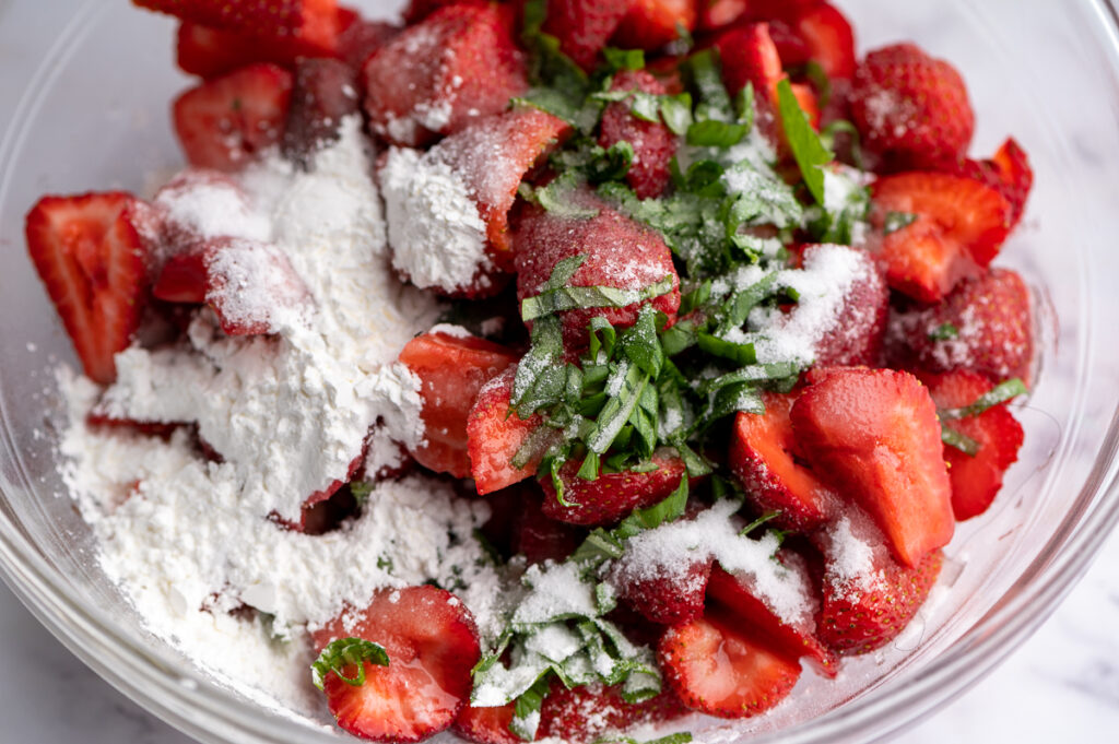 Sliced strawberries, sliced basil, and sugar and starch in a bowl.